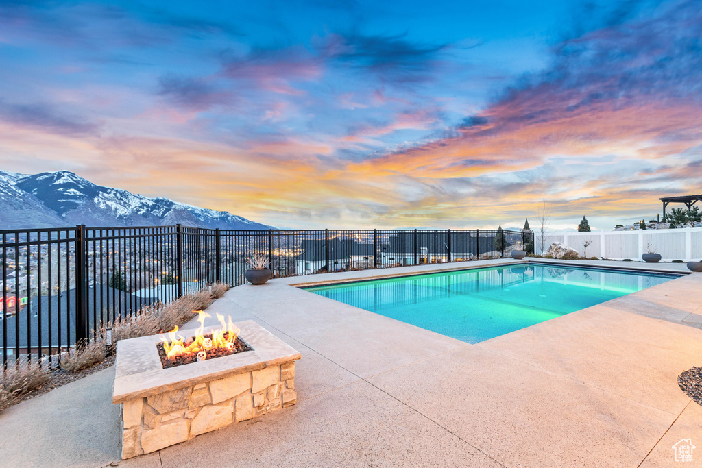 Pool at dusk with a mountain view, a patio area, and an outdoor fire pit