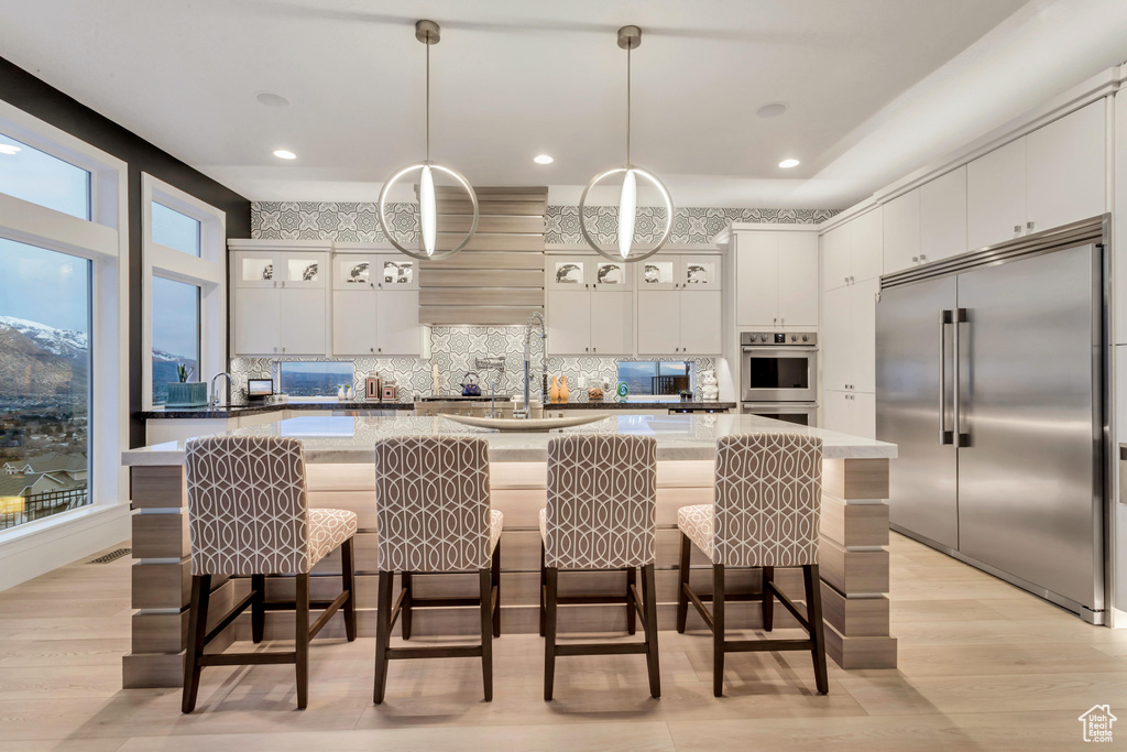 Kitchen with white cabinets, appliances with stainless steel finishes, a kitchen island with sink, and a wealth of natural light