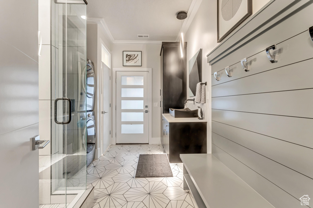 Mudroom featuring stacked washer and dryer, light tile floors, and ornamental molding