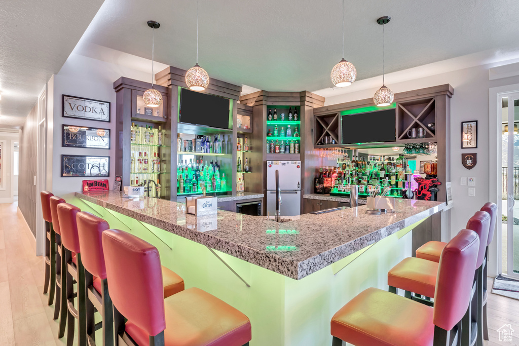 Bar with light hardwood / wood-style flooring, decorative light fixtures, and stainless steel fridge