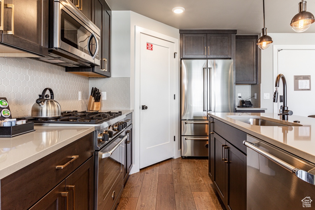 Kitchen with high quality appliances, dark brown cabinetry, decorative light fixtures, tasteful backsplash, and dark wood-type flooring