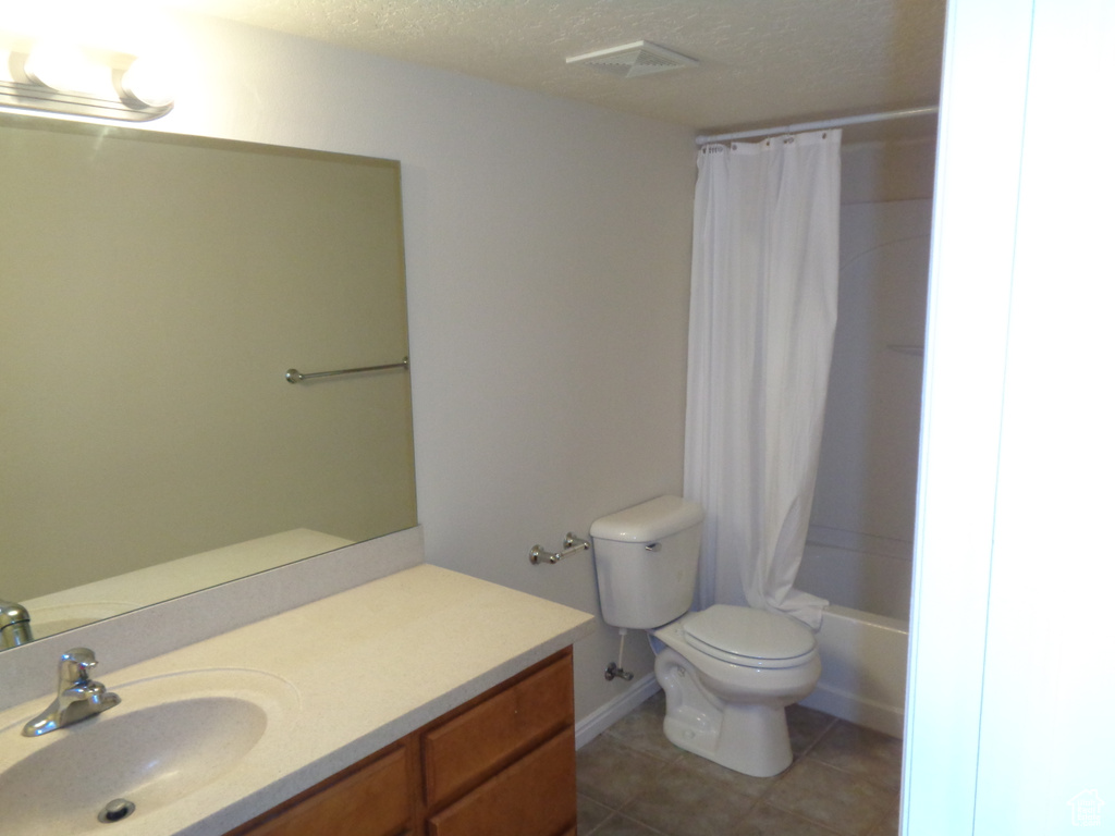 Full bathroom with tile floors, toilet, oversized vanity, shower / bathtub combination with curtain, and a textured ceiling