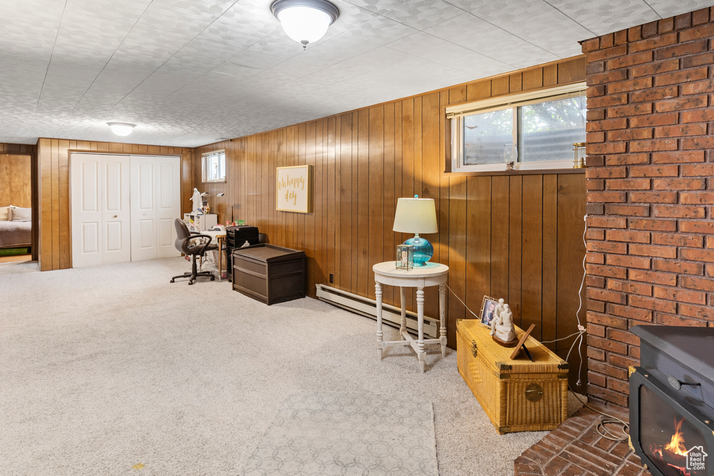 Living area with a baseboard radiator, wooden walls, a wood stove, carpet floors, and brick wall