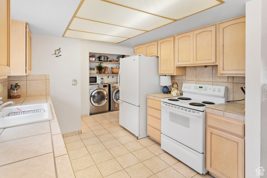 Kitchen featuring tile countertops, washer and clothes dryer, tasteful backsplash, white appliances, and light brown cabinetry