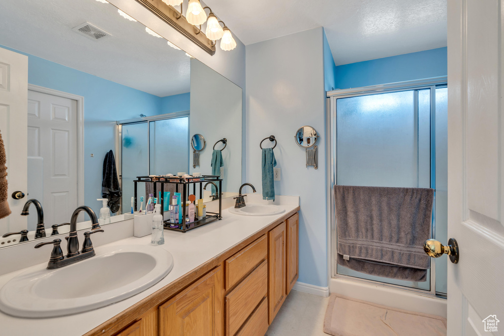 Bathroom featuring double sink vanity, a shower with shower door, and tile floors