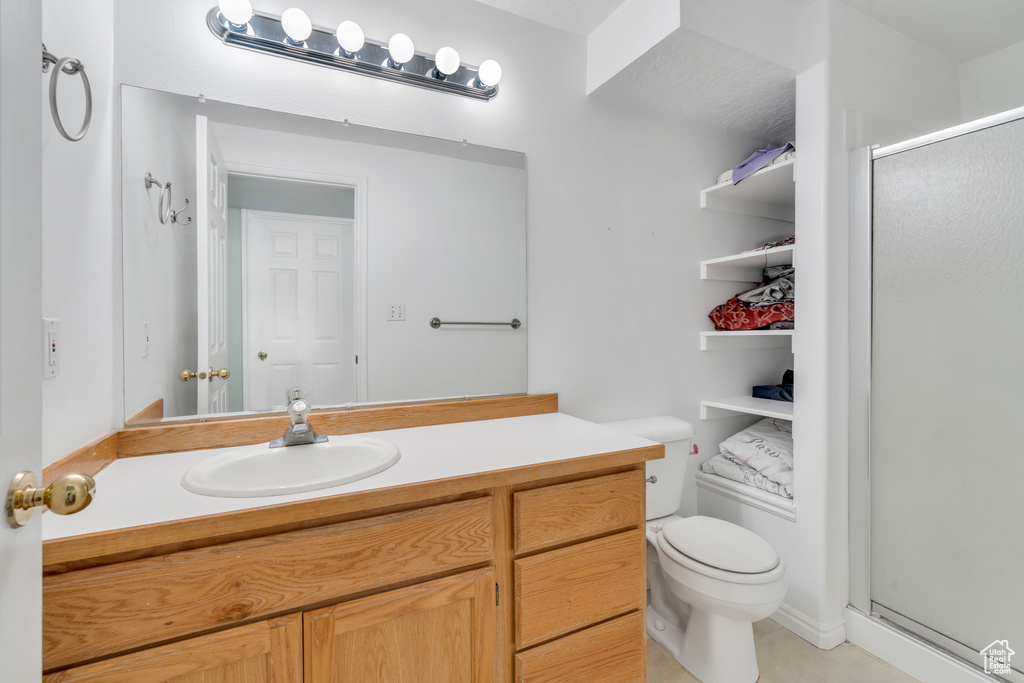Bathroom with an enclosed shower, vanity with extensive cabinet space, tile flooring, and toilet