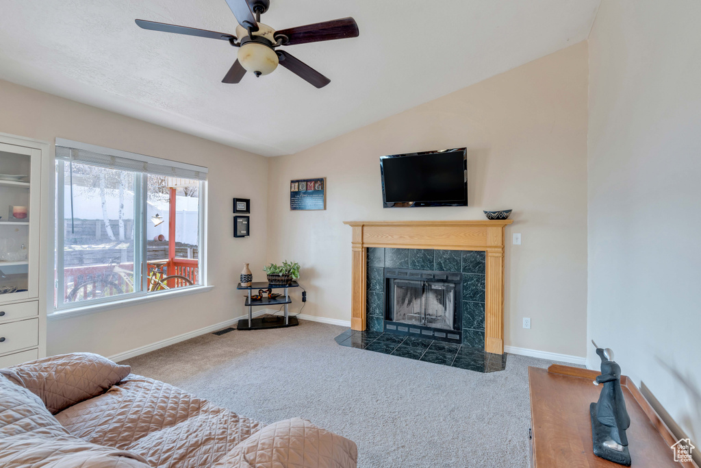Living room featuring vaulted ceiling, a tiled fireplace, carpet, and ceiling fan