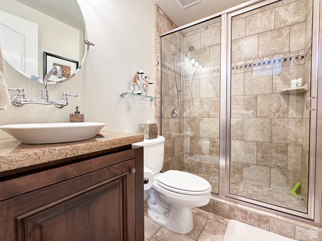 Bathroom featuring a shower with shower door, tile floors, vanity, and toilet