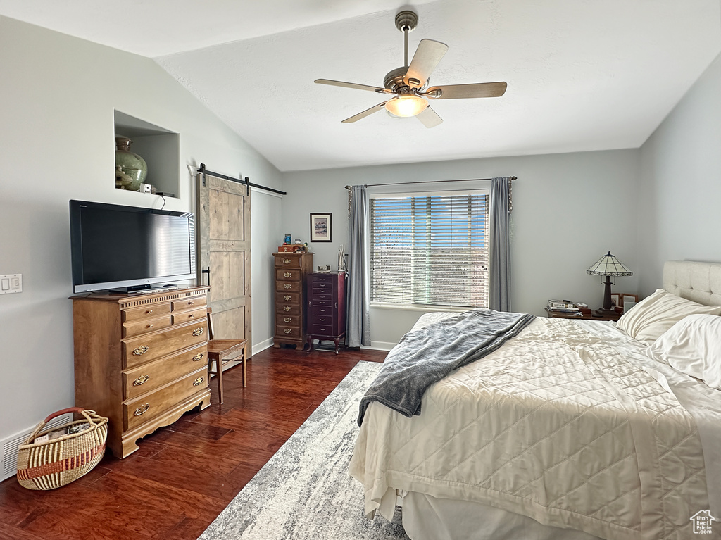 Bedroom with dark hardwood / wood-style flooring, a barn door, vaulted ceiling, and ceiling fan
