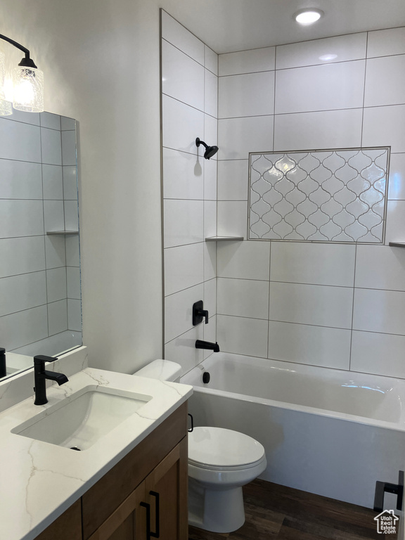 Full bathroom with toilet, tiled shower / bath combo, large vanity, and hardwood / wood-style flooring