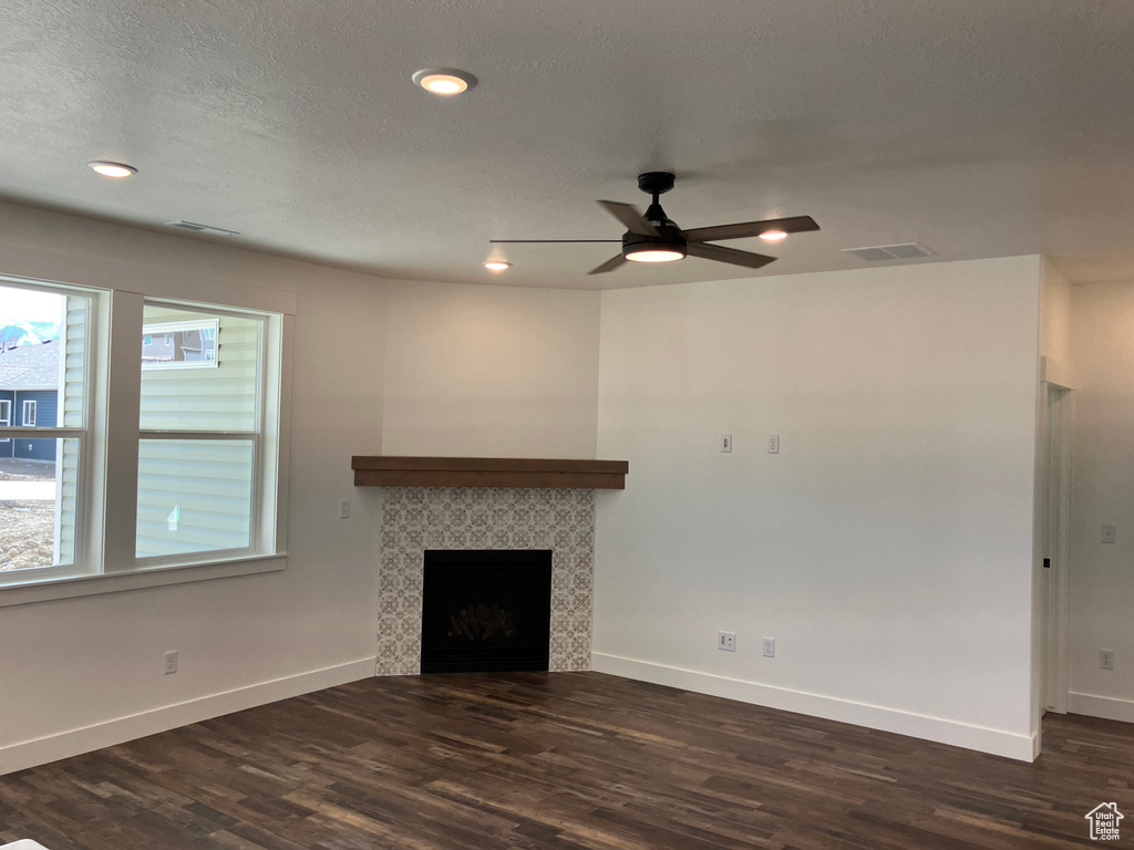 Unfurnished living room featuring a textured ceiling, ceiling fan, a tile fireplace, and dark hardwood / wood-style flooring