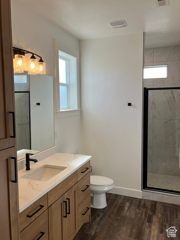 Bathroom featuring a tile shower, hardwood / wood-style floors, vanity, and toilet