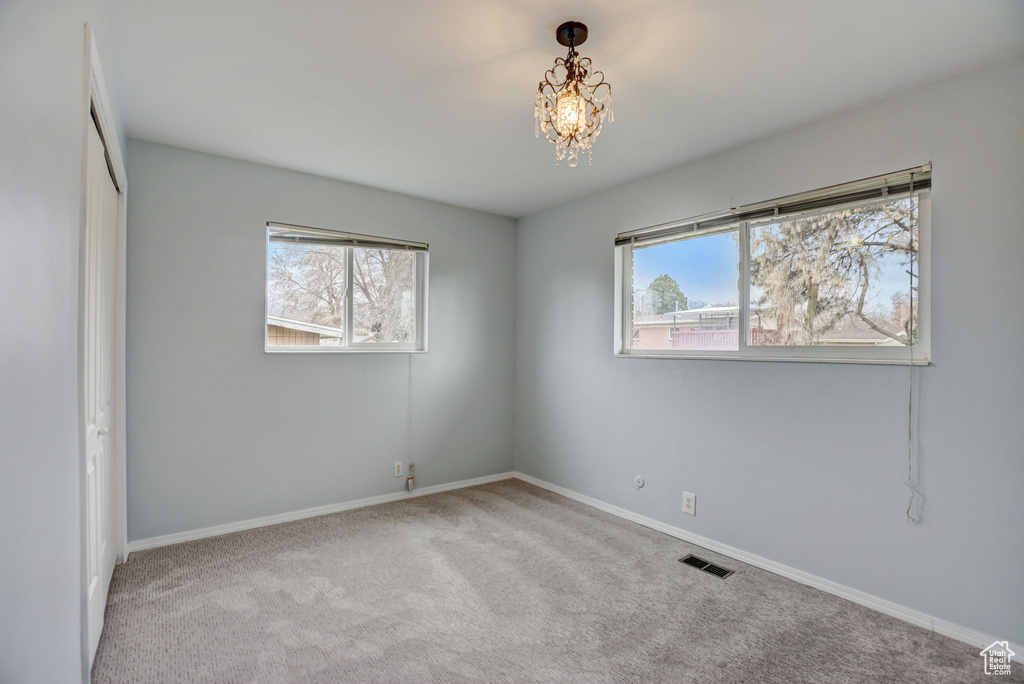 Unfurnished room with an inviting chandelier and light carpet