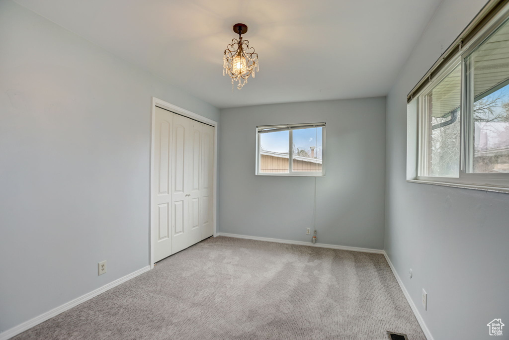 Unfurnished bedroom featuring a closet, light colored carpet, and a chandelier