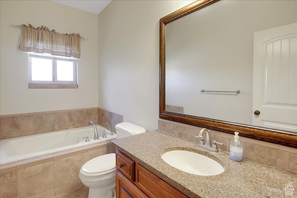 Bathroom featuring tiled tub, vanity with extensive cabinet space, and toilet