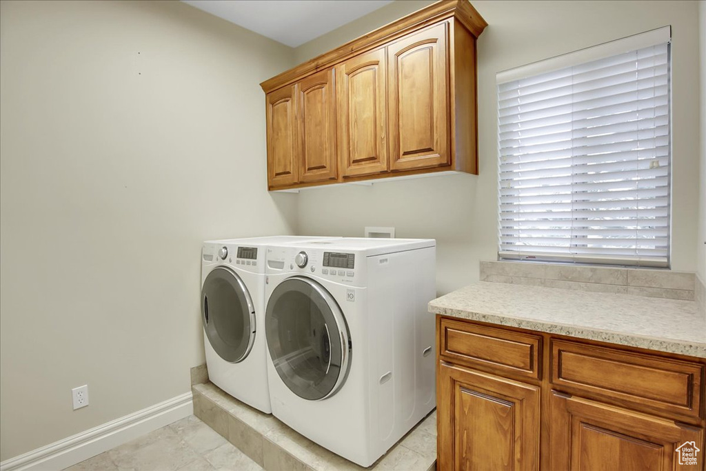 Laundry area with a healthy amount of sunlight, washer and clothes dryer, cabinets, and light tile floors