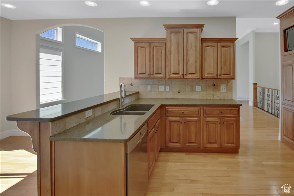 Kitchen featuring dishwasher, light stone countertops, sink, tasteful backsplash, and light hardwood / wood-style flooring
