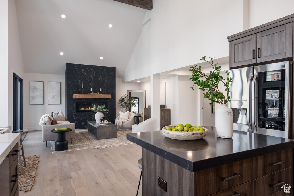 Kitchen featuring high vaulted ceiling, dark brown cabinetry, light hardwood / wood-style floors, and a fireplace