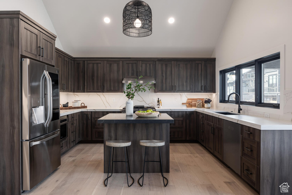 Kitchen featuring light hardwood / wood-style floors, stainless steel appliances, a center island, sink, and lofted ceiling