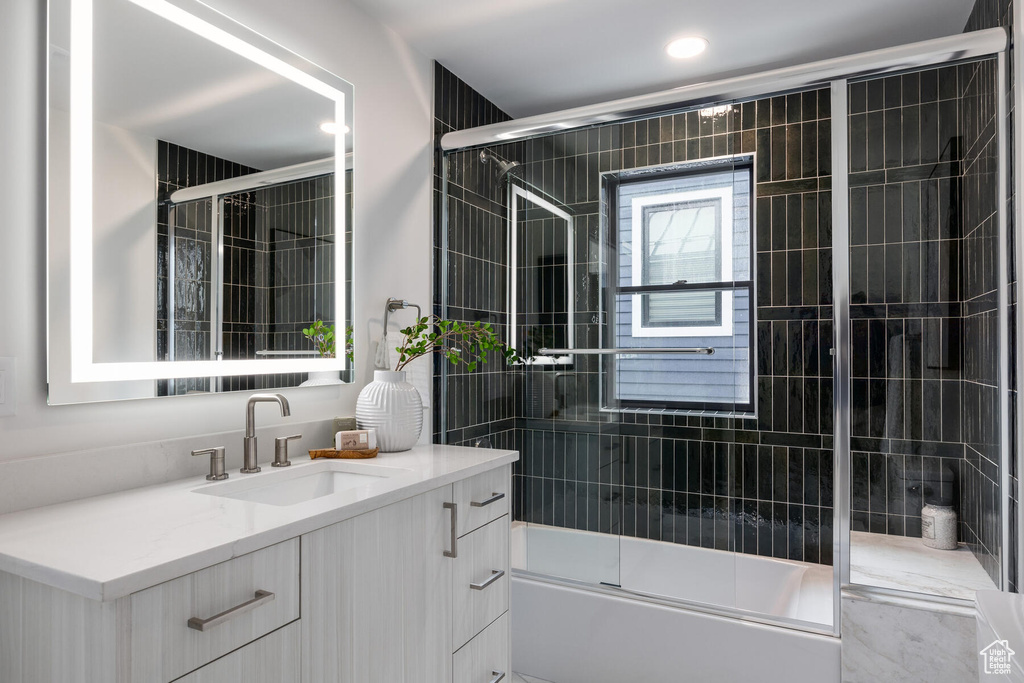 Bathroom with vanity and bath / shower combo with glass door