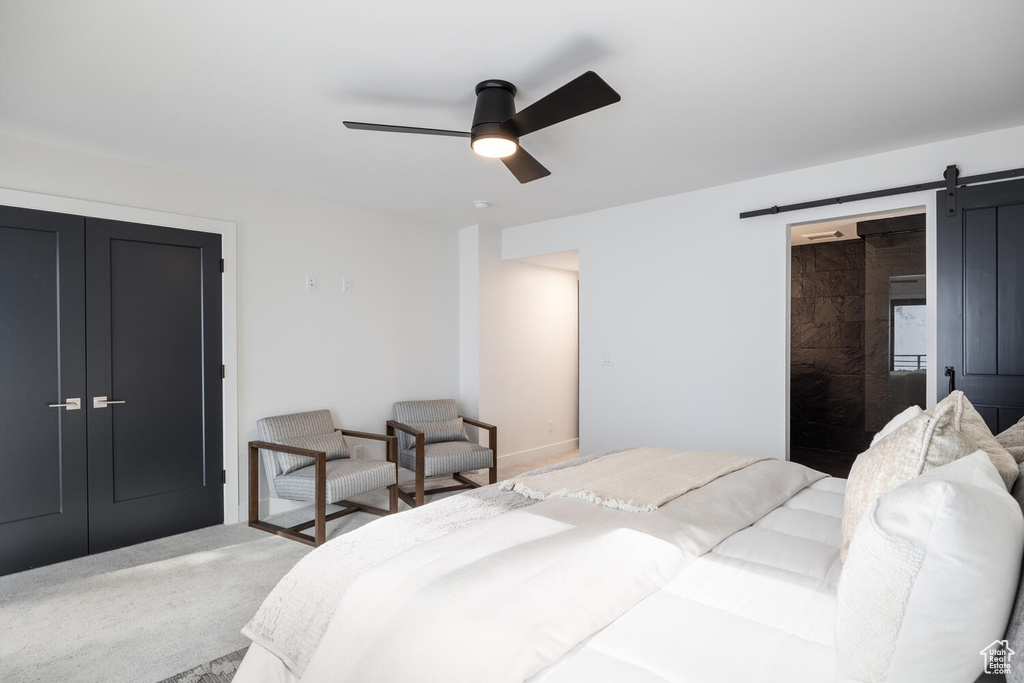 Carpeted bedroom featuring a barn door, ceiling fan, and a closet