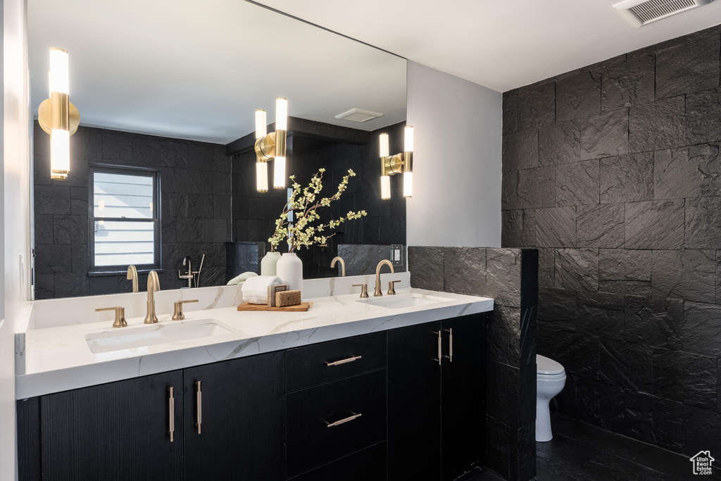 Bathroom with toilet, double sink vanity, and tile walls