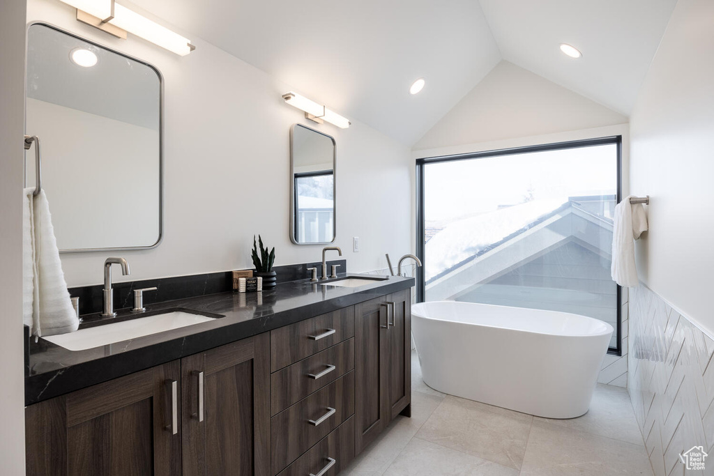 Bathroom with tile floors, vanity with extensive cabinet space, a bathing tub, vaulted ceiling, and dual sinks