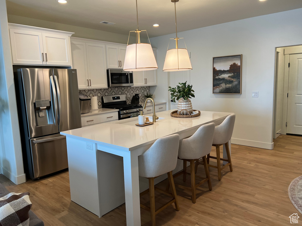 Kitchen with backsplash, a center island with sink, stainless steel appliances, and light hardwood / wood-style flooring