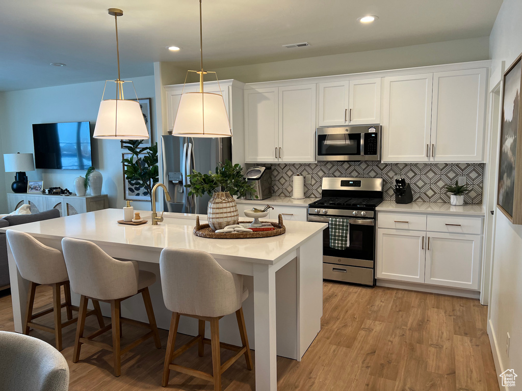 Kitchen featuring decorative light fixtures, light hardwood / wood-style flooring, white cabinetry, and stainless steel appliances