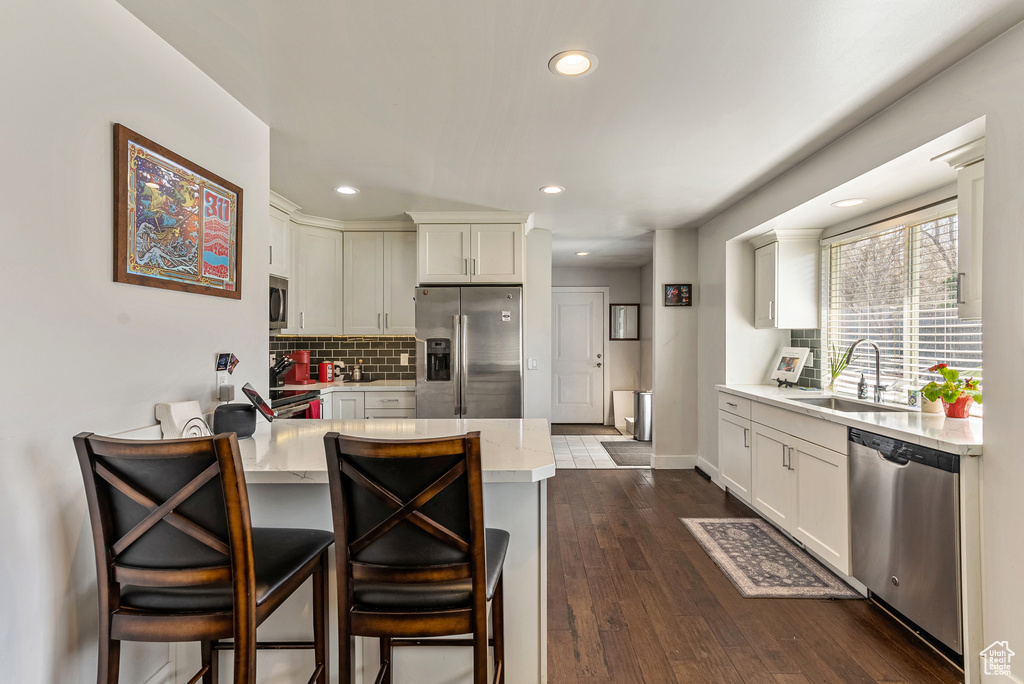 Kitchen featuring backsplash, sink, appliances with stainless steel finishes, dark hardwood / wood-style flooring, and a kitchen bar