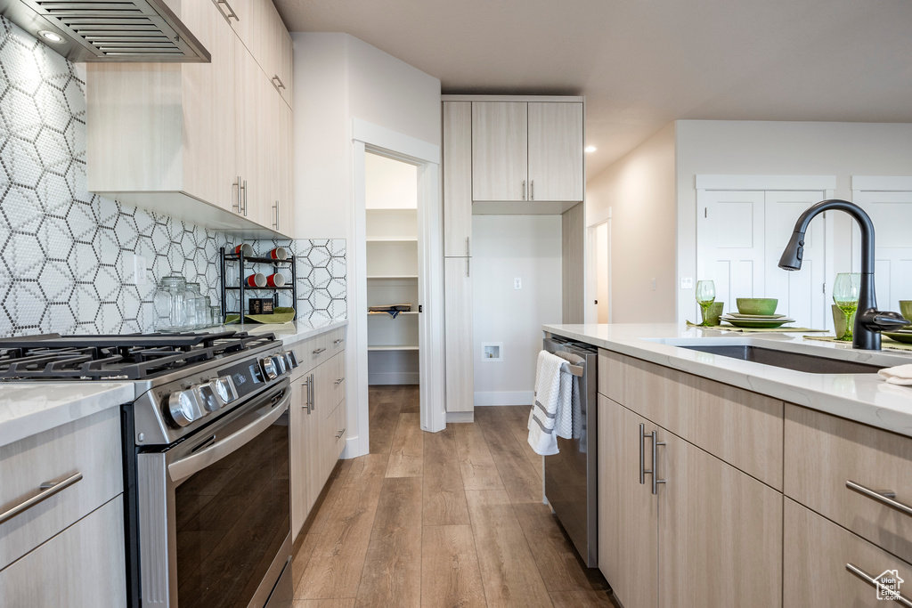 Kitchen featuring appliances with stainless steel finishes, sink, backsplash, light hardwood / wood-style flooring, and premium range hood