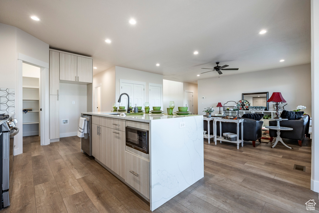 Kitchen featuring appliances with stainless steel finishes, wood-type flooring, sink, and an island with sink