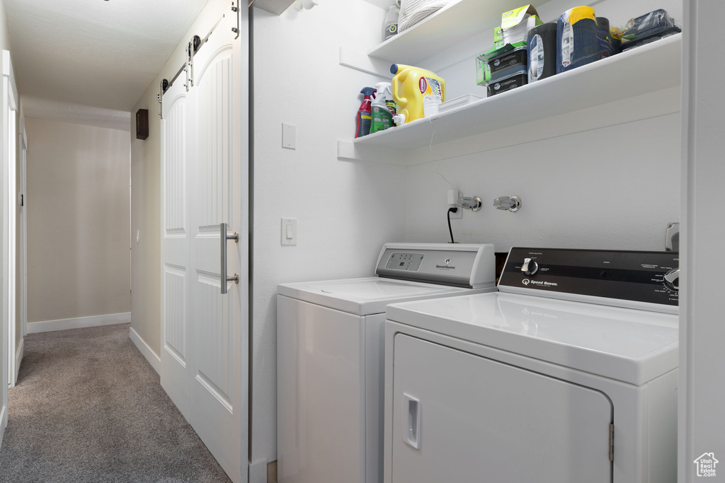 Laundry area with a barn door, light colored carpet, and washing machine and clothes dryer