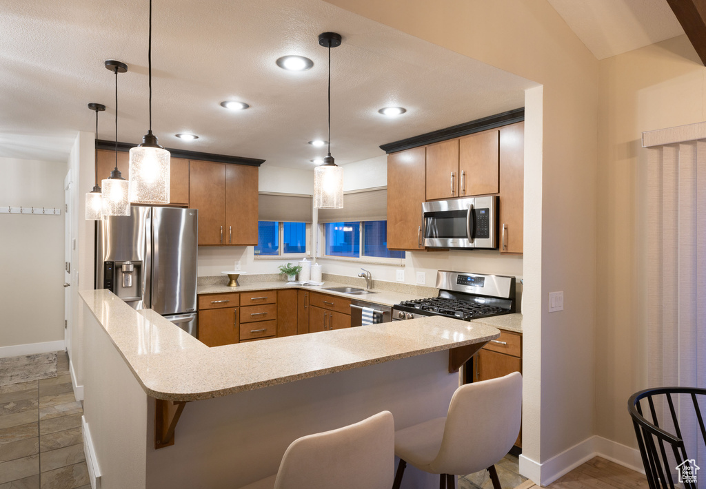 Kitchen featuring kitchen peninsula, a kitchen breakfast bar, pendant lighting, sink, and appliances with stainless steel finishes
