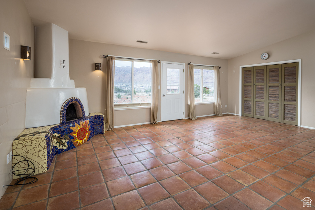 Unfurnished living room featuring a brick fireplace, vaulted ceiling, and dark tile floors