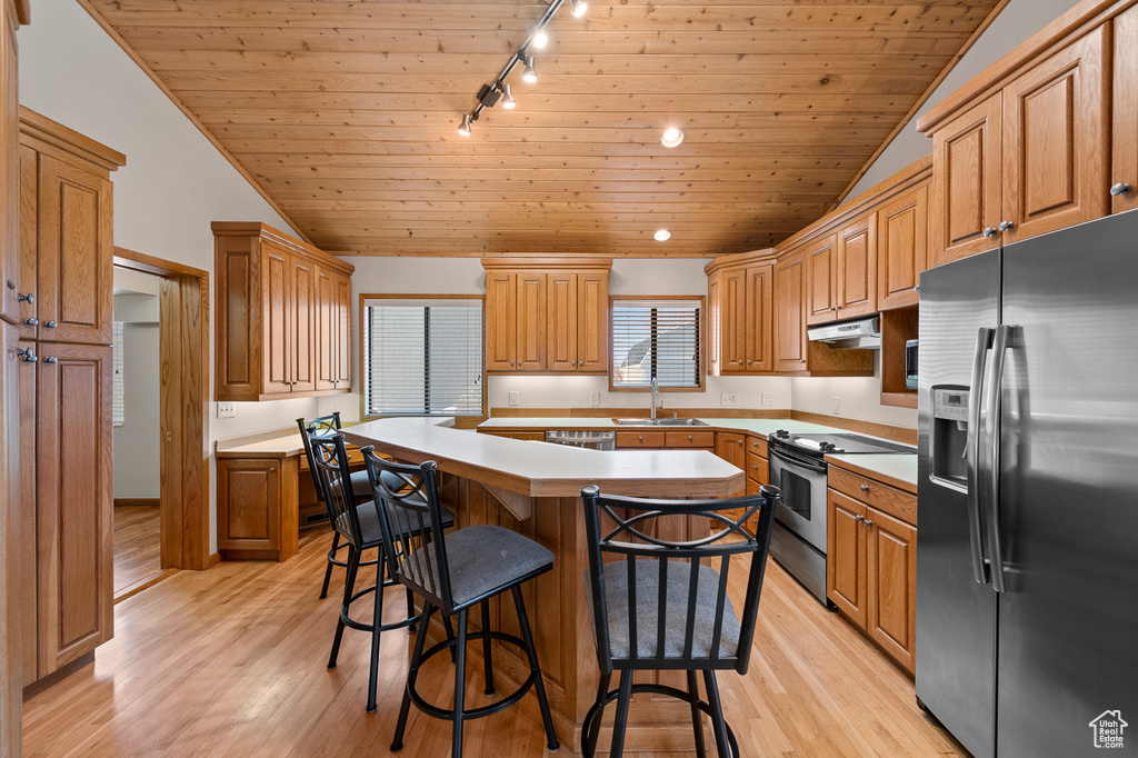 Kitchen featuring appliances with stainless steel finishes, a kitchen island, track lighting, vaulted ceiling, and light hardwood / wood-style floors