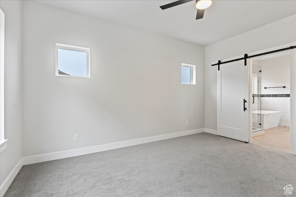 Unfurnished bedroom with a barn door, connected bathroom, ceiling fan, and light colored carpet
