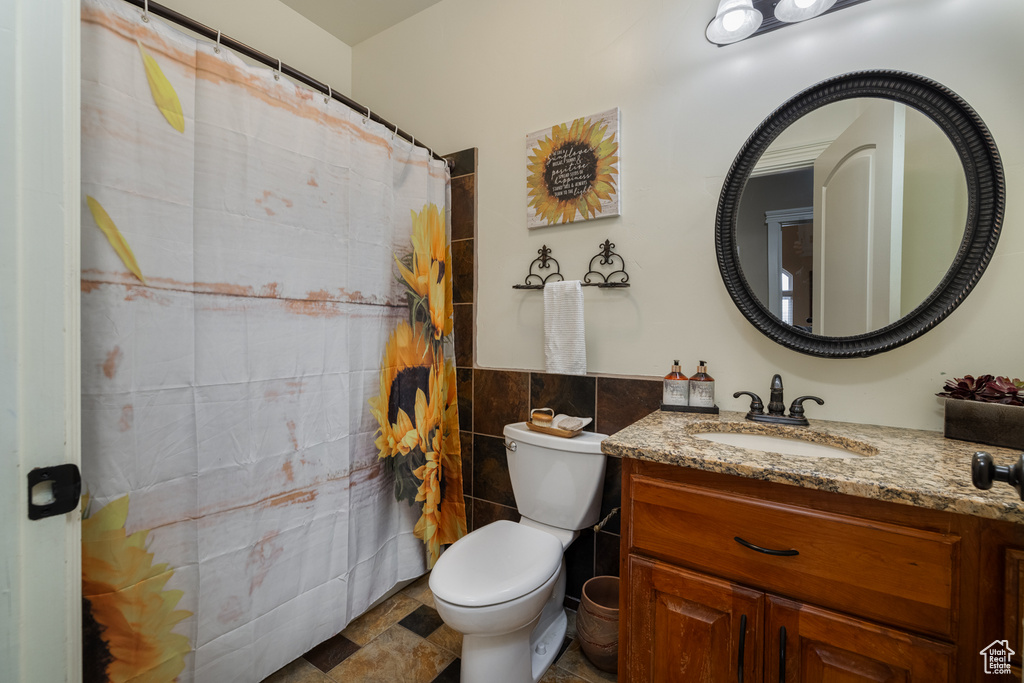 Bathroom with tile flooring, tile walls, oversized vanity, and toilet