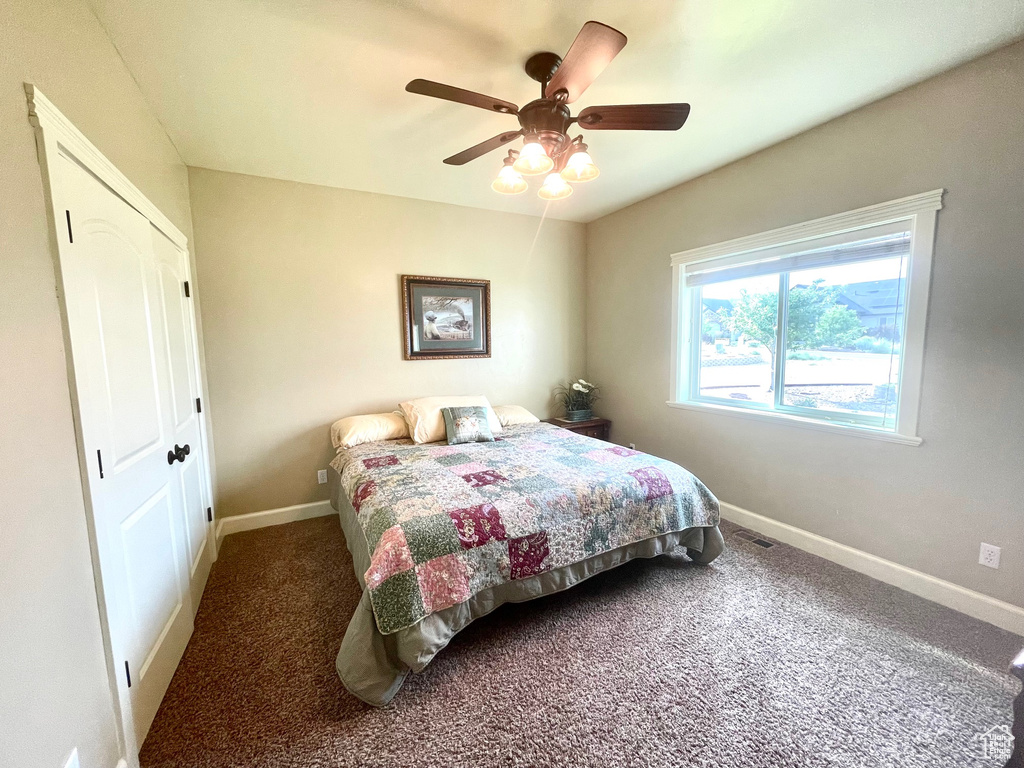 Bedroom with a closet, dark carpet, and ceiling fan