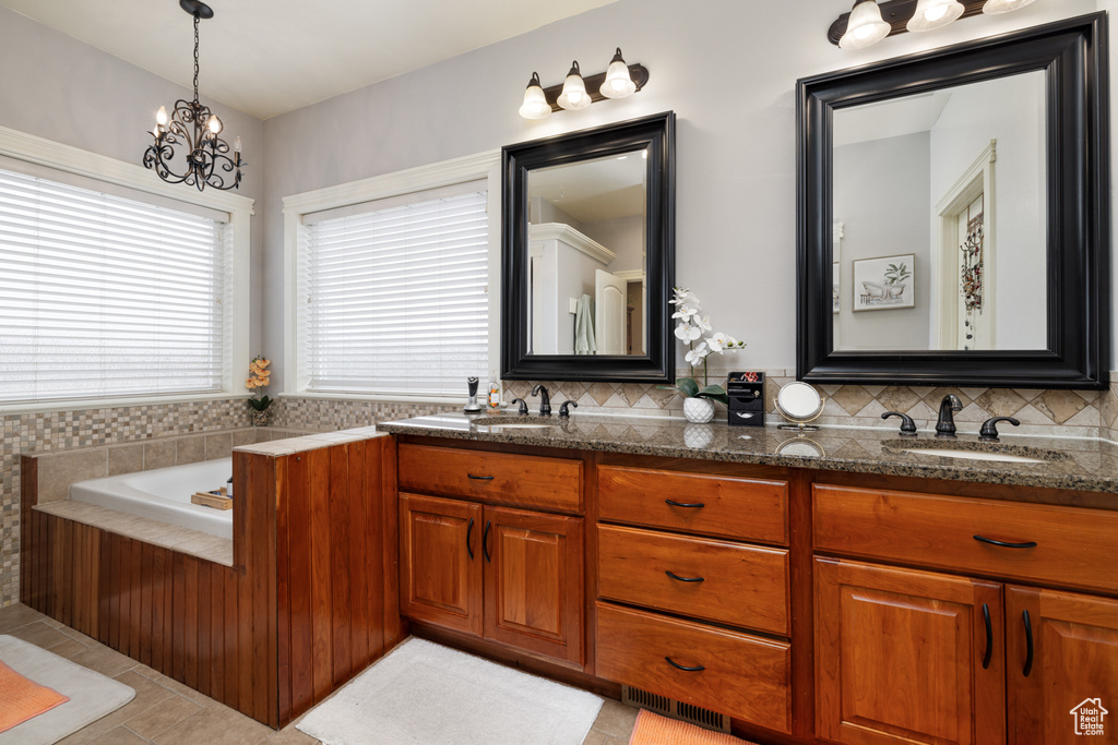 Bathroom featuring backsplash, a chandelier, a relaxing tiled bath, tile floors, and dual vanity