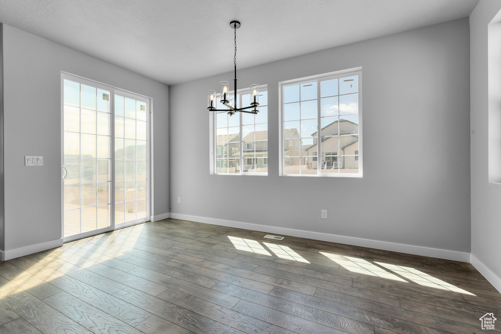 Empty room with hardwood / wood-style floors and a notable chandelier