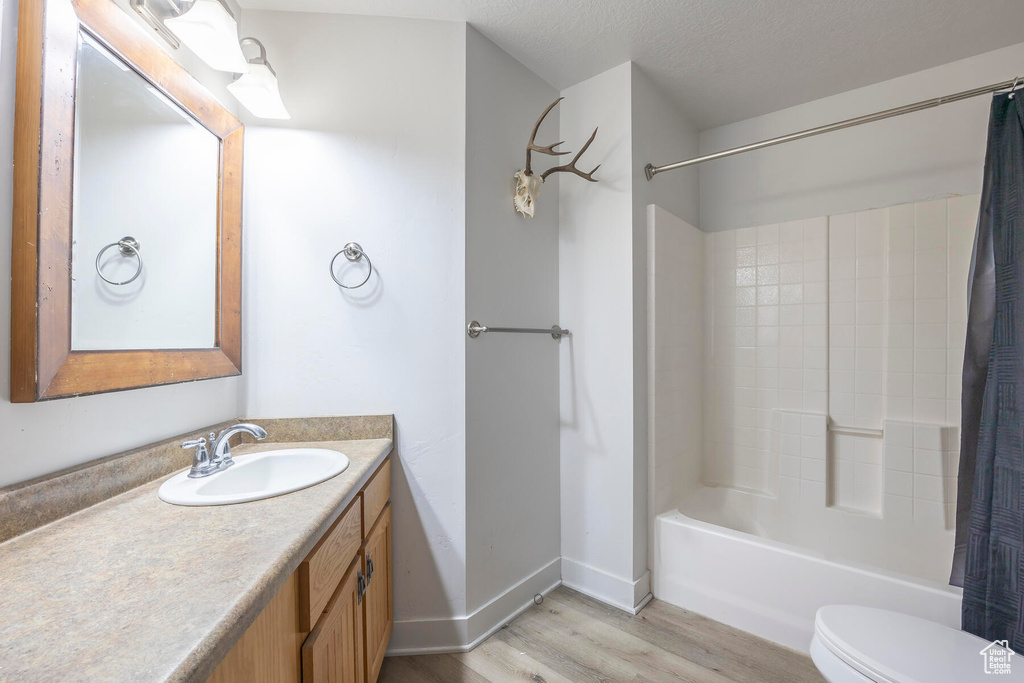 Full bathroom with wood-type flooring, a textured ceiling, shower / tub combo with curtain, large vanity, and toilet
