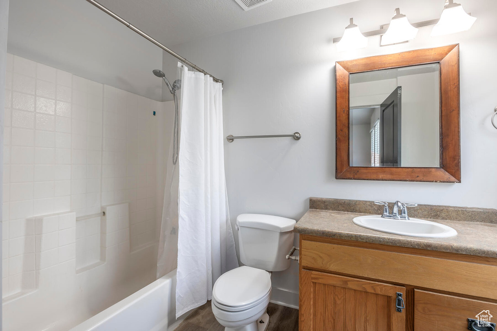 Full bathroom featuring hardwood / wood-style floors, vanity, a textured ceiling, shower / bathtub combination with curtain, and toilet
