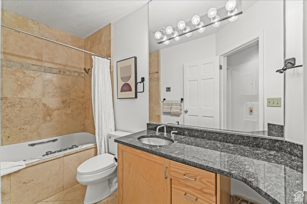 Full bathroom with shower / bath combo, tile floors, large vanity, toilet, and a textured ceiling
