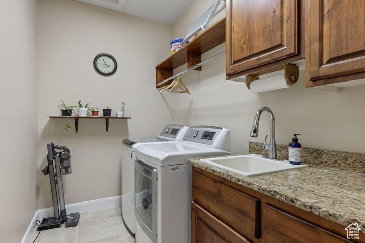Clothes washing area featuring sink, cabinets, washing machine and clothes dryer, and light tile flooring