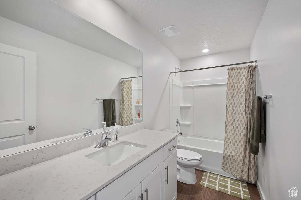 Full bathroom featuring large vanity, shower / bath combination with curtain, a textured ceiling, toilet, and tile floors