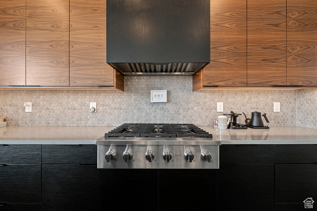 Kitchen featuring custom exhaust hood, backsplash, and stainless steel gas cooktop