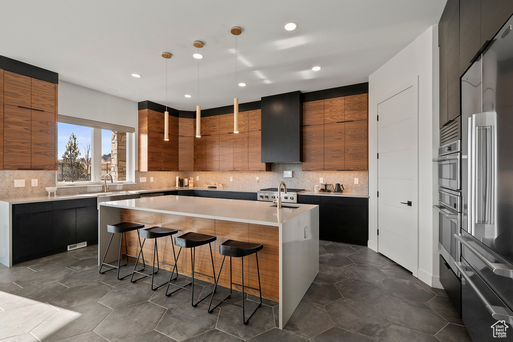 Kitchen featuring pendant lighting, backsplash, sink, an island with sink, and a kitchen bar