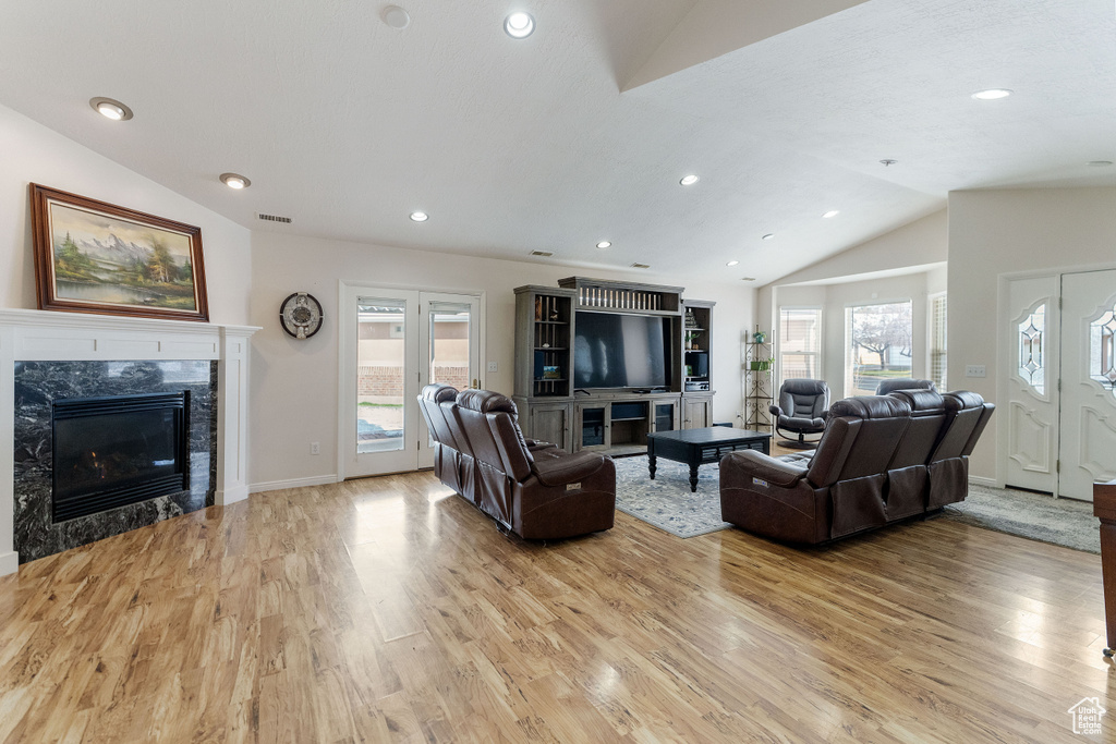 Living room with light hardwood / wood-style flooring, lofted ceiling, plenty of natural light, and a premium fireplace