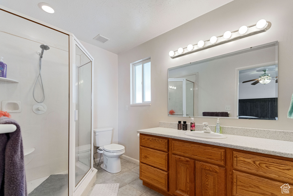Bathroom featuring ceiling fan, tile flooring, an enclosed shower, vanity, and toilet